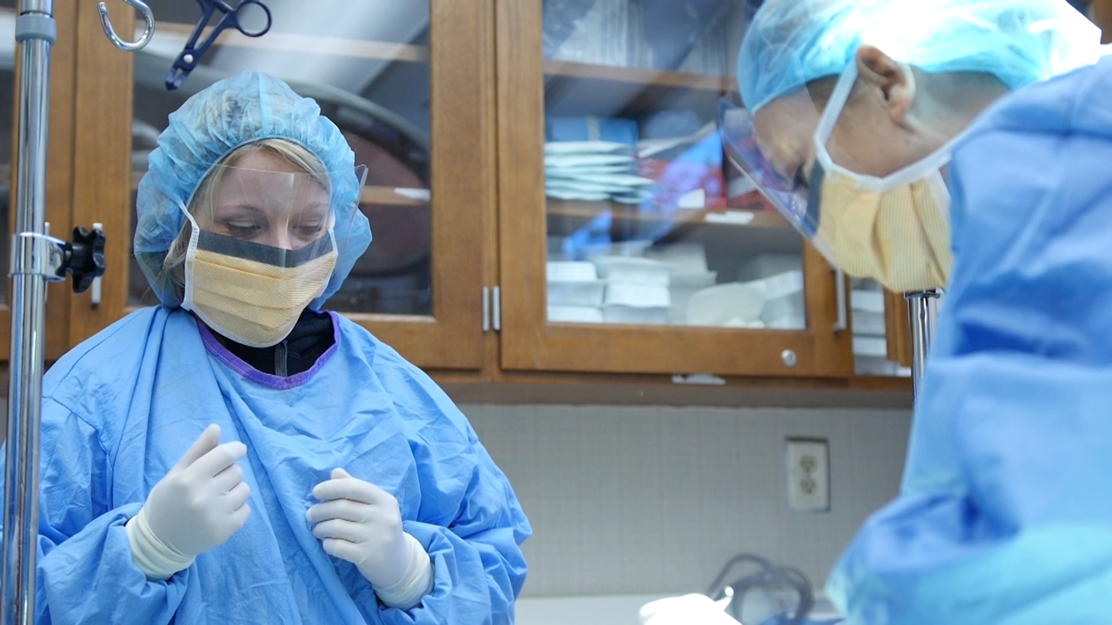 Two students dressed in scrubs and masks practice surgical techniques.